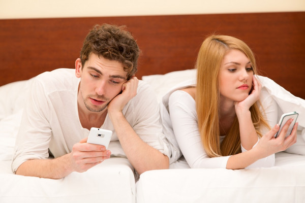 Mann-und-Frau-die-ihre-Handysucht-bekaempfen-sollten-liegen-im-Bett-und-sehen-jeweils-auf-ihr-Smartphone